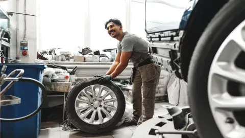 Werkstattmitarbeiter hebt Autoreifen in moderner Werkstatt