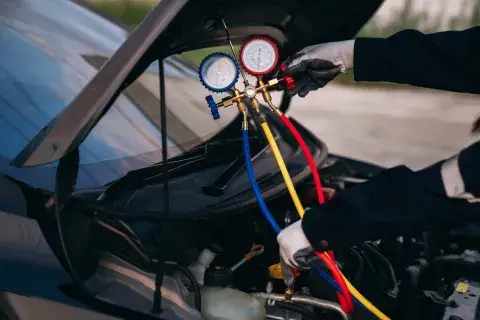 Kfz-Mechaniker überprüft Klimaanlage mit Manometern unter der Motorhaube