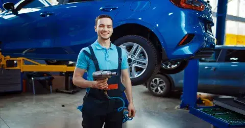 Mechaniker mit Werkzeug vor einem angehobenen blauen Auto in der Werkstatt